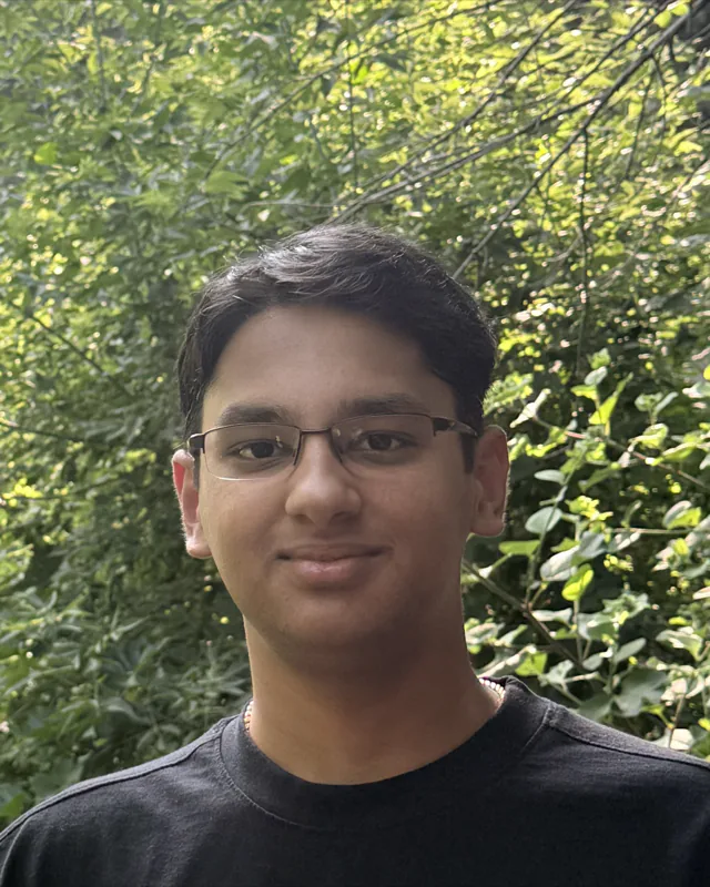 Shankar Krishnamurthy, smiling, in front of green leaves.
